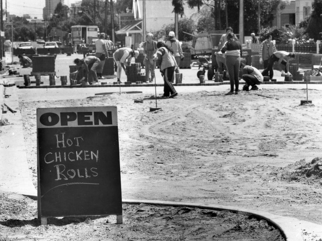 A signboard for a food shop stand far out on the footpath as road workers rebuild King William Rd in the background on October 30, 1985. Source: File