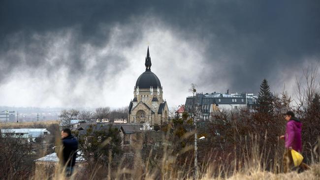 People walk in front of a church as smoke rises after an air strike in the western Ukrainian city of Lviv on March 26. Picture: AFP