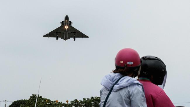 Two people ride a motorcycle as a Taiwanese Air Force Mirage 2000 fighter jet approaches.