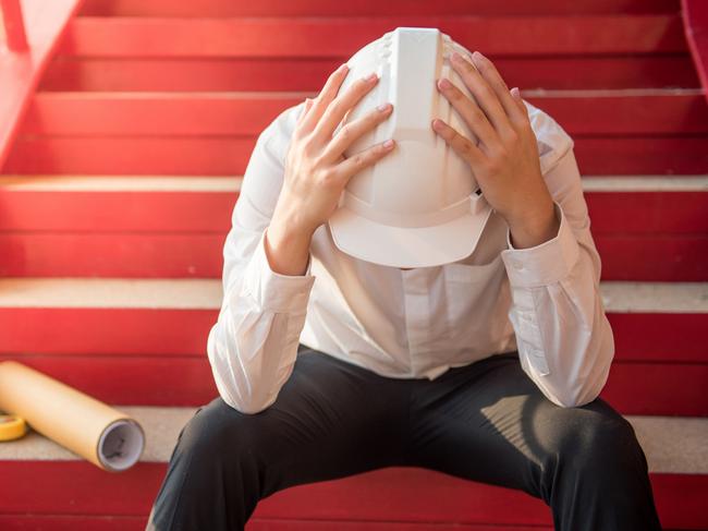 Engineer or Architect feeling tired and headache with his job. sitting on building stairs with architectural drawing on his side while wearing protective equipment safety helmet at construction site - Photo Supplied Istock