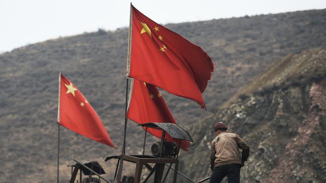 Chinese flags next to a worker clearing a conveyor belt used to transport coal, near a coal mine at Datong, in China's northern Shanxi province. Picture: Greg Baker