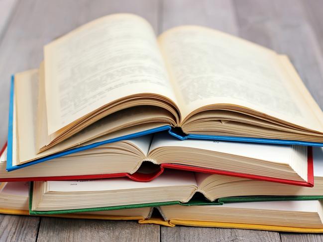 Four open books in the colored cover on the table made of boards.A stack of books in the colored covers on the table with a red tablecloth. Still life with books. iStock image