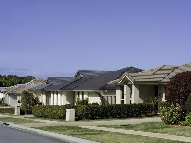 Suburban australian street in new housing estate, showing brick and tile real estate and gardens.