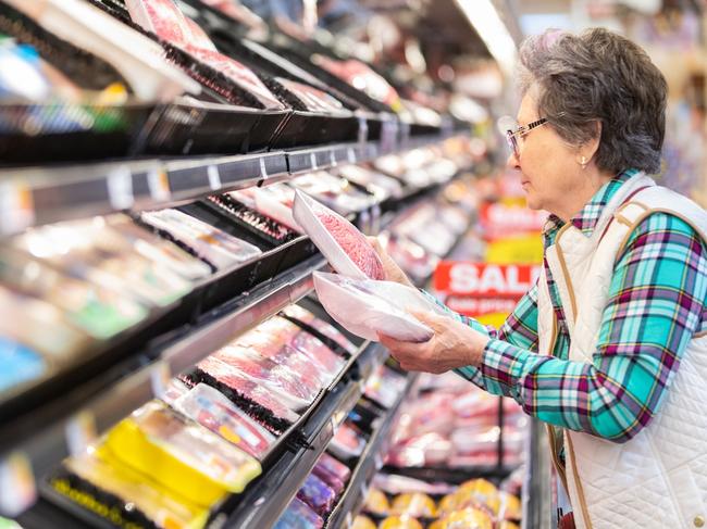 Senior woman comparing prices for meat selection.