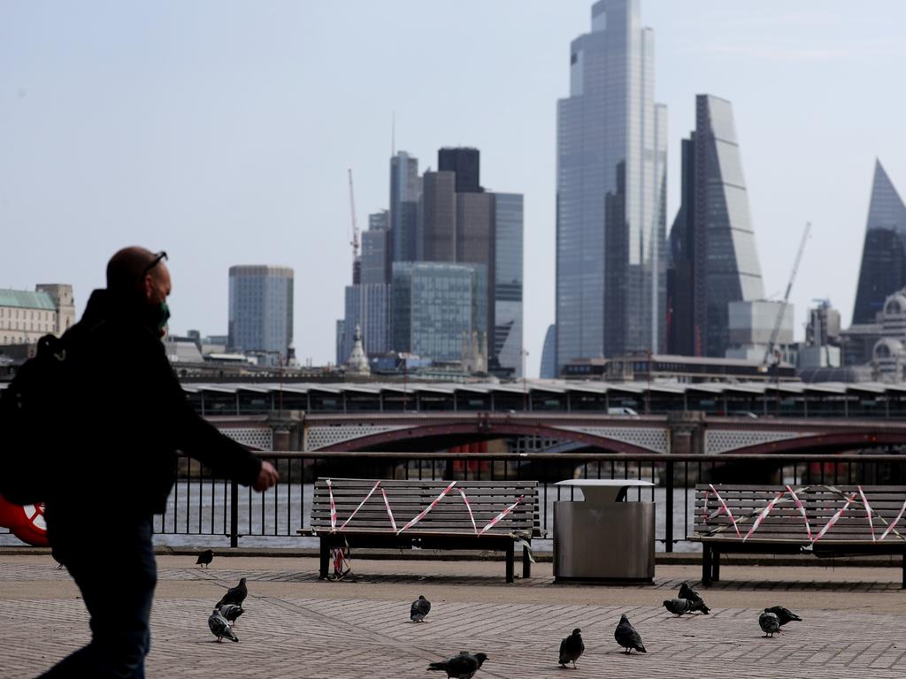A man with a protective face mask passes taped off benches that should help people to keep their social distance during the coronavirus lockdown in London. Picture: AP