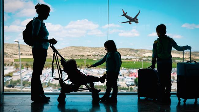 Mother with kids and luggage looking at planes in airport, family travel. istock image