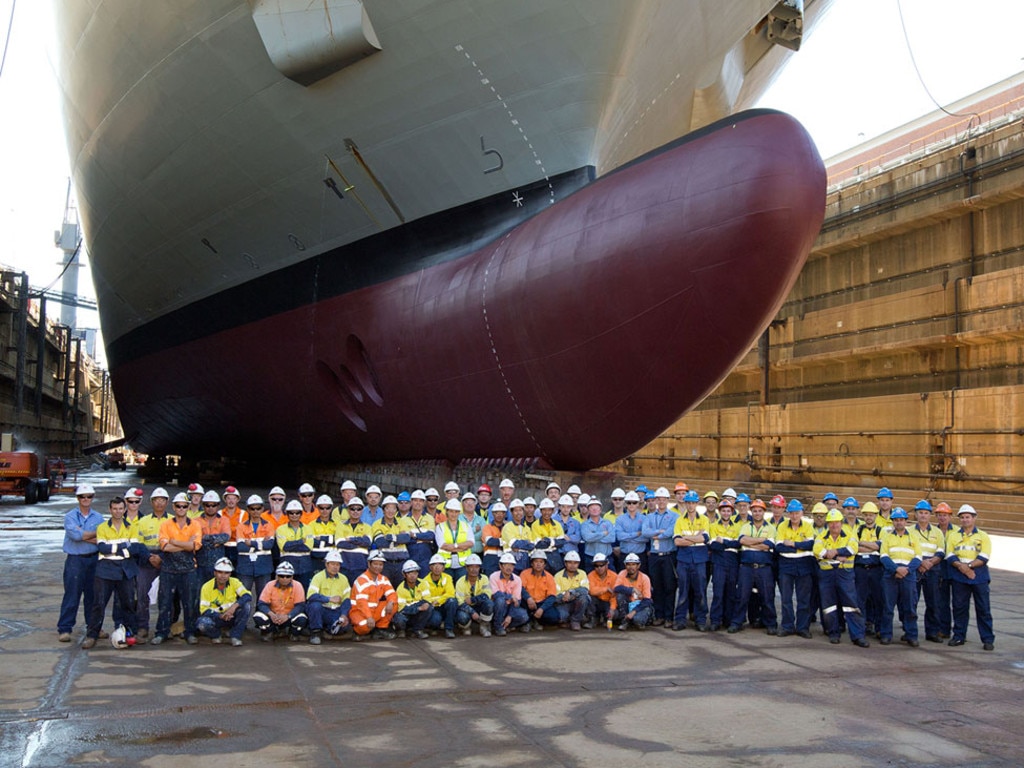 Group photo of BAE Systems employees under the hull of Nuship Canberra in the dry dock at Fleet Base East, Garden Island, Sydney, NSW.