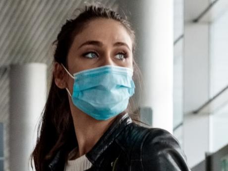 People traveling by plane during COVID 19. Young woman wearing N95 face masks, sitting on luggage in airport terminal, holding smart phone.Photo - istockEscape 17 July 2022doc holiday