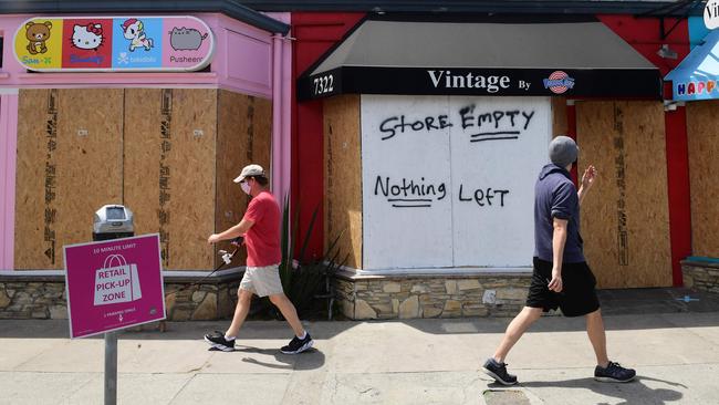 Pedestrians walk past boarded up storefronts on Melrose Avenue in Los Angeles.