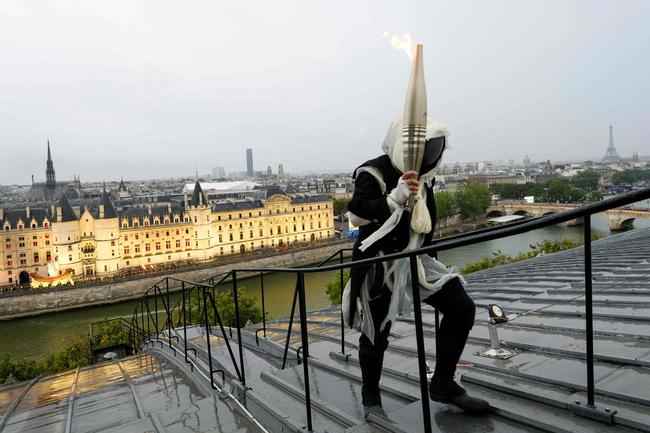 A torchbearer carries the Olympic flame over a building along the Seine River in Paris, France, during the opening ceremony for the 2024 Summer Olympics, Friday, July 26, 2024. (Photo by Bernat Armangue / POOL / AFP)