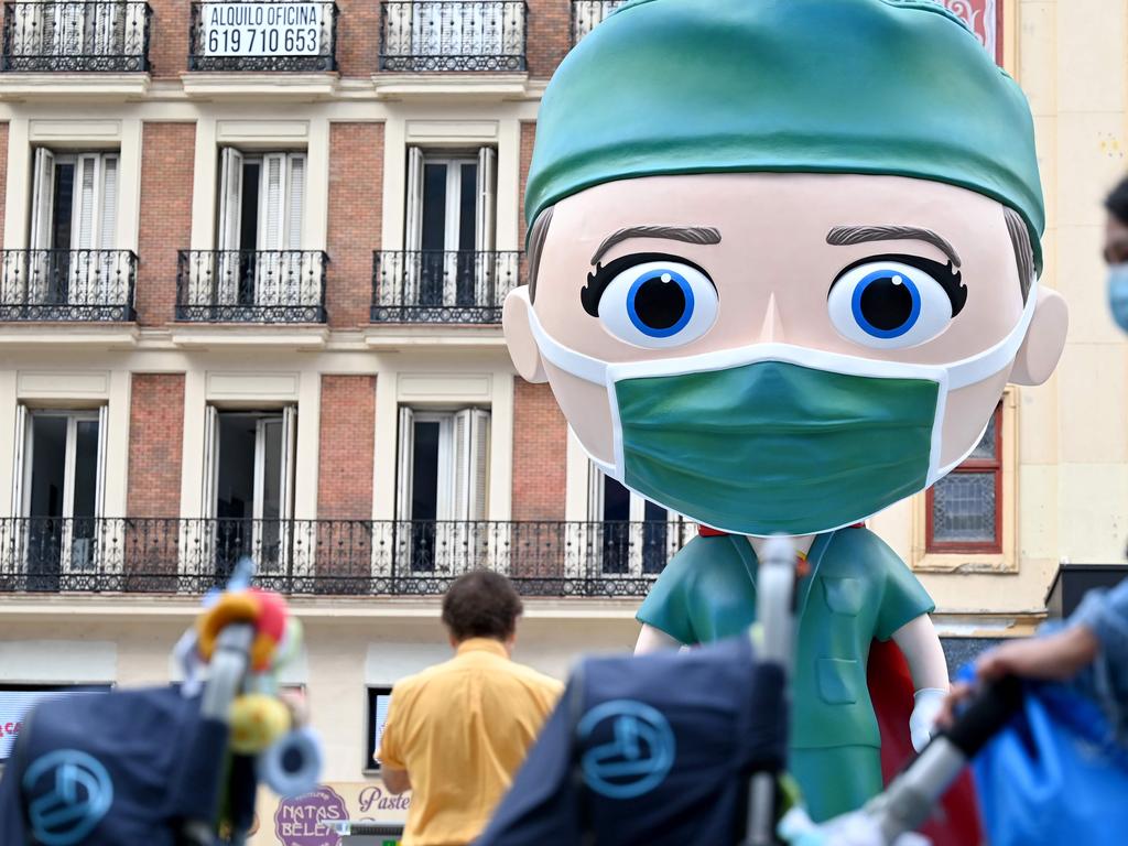 People wearing face masks walk on September 24, 2020 by a 6 meters high statue depecting a "Superhealthworker"  installed in Madrid to pay tribute to the heroes who fight against coronavirus. (Photo by Gabriel BOUYS / AFP)