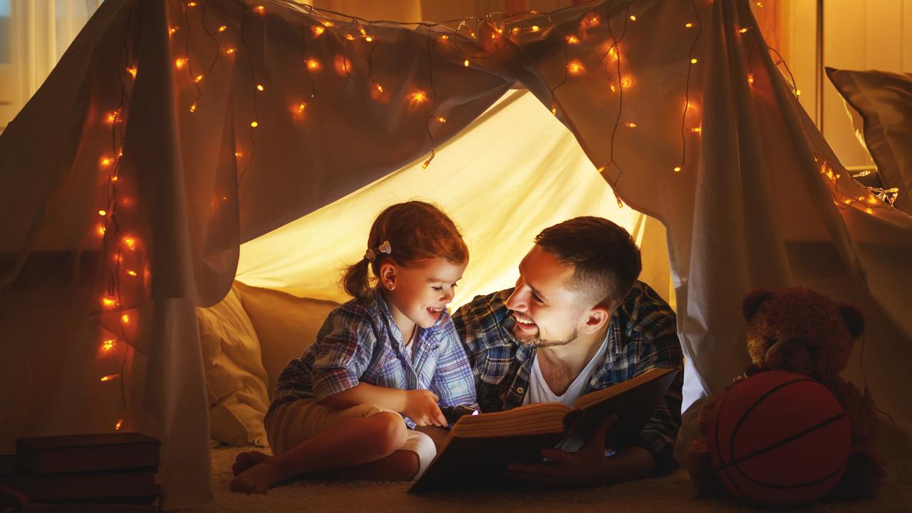 happy family father and child daughter reading a book  in  tent at home