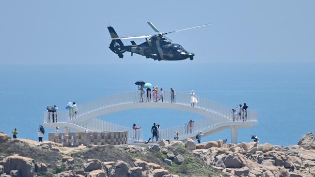 Tourists look on as a Chinese military helicopter flies past Pingtan island, one of mainland China's closest point from Taiwan. Picture: AFP