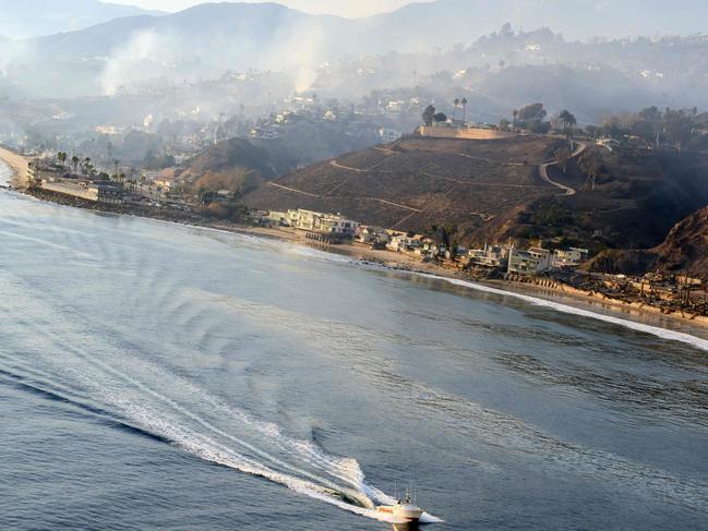 In this aerial view taken from a helicopter, a lifeguard boat motors past burned homes on Pacific Coast Highway during the Palisades fire in Malibu, California, on January 9, 2025. The two largest fires burning in Los Angeles remain 
