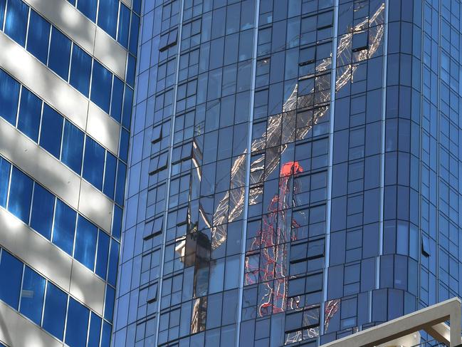 Two cranes are reflected on the side of a high-rise building in Melbourne on May 5, 2020. - Australia's economy is losing 4 billion Australian dollars (2.5 billion USD) every week its virus shutdown continues, while a million workers have already lost their jobs in the crisis, according to figures announced on May 5. (Photo by William WEST / AFP)