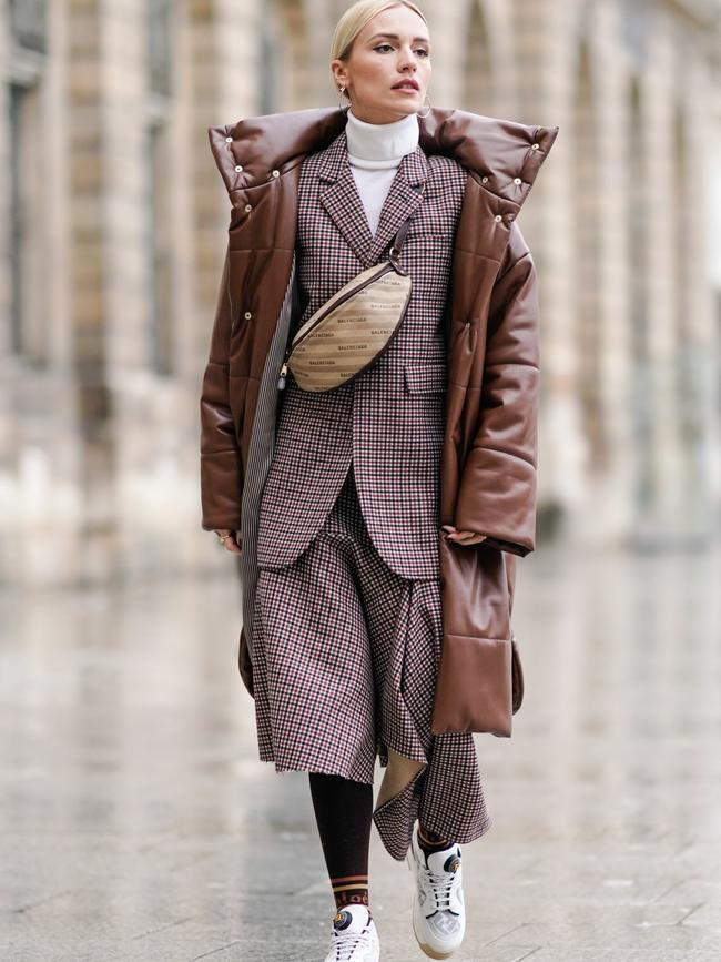 A guest wears a brown long puffer coat, a Balenciaga fanny pack bag, a checked blazer jacket, and a white turtleneck, outside the Alexis Mabille show during Paris Fashion Week. Picture: Getty Images