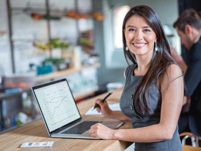 Happy business woman working at a cafe on a laptop and looking at the camera smiling. Image on screen is own design. Investor generic