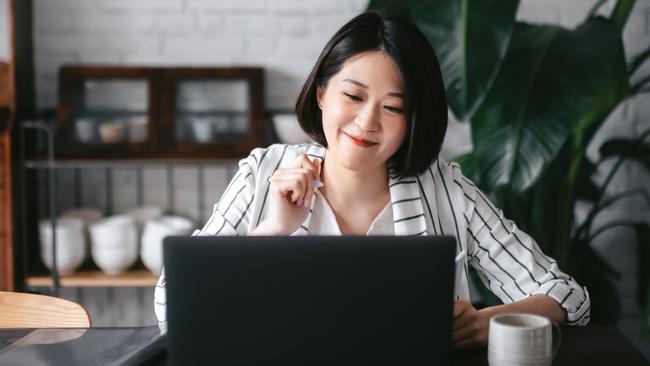 Young Asian woman having online business meeting, video conferencing on laptop with her business partners, working from home in the living room