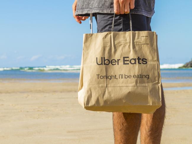 Gold Coast, Australia - May 5, 2019: Customer with Uber Eats' bag in a paradise beach in the middle of nowhere in Gold Coast area.