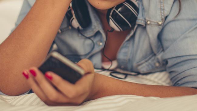 Teenage girl lying on bed in her room and checking smart phone.