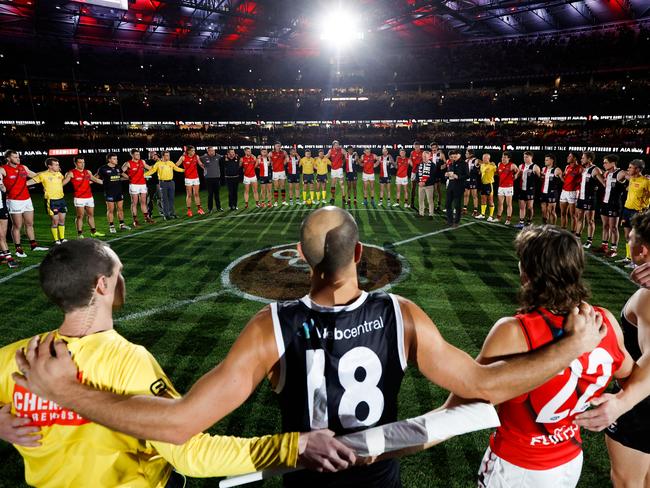 MELBOURNE, AUSTRALIA - JUNE 17: Players, coaches and umpires huddle as Tim Watson and Nathan Burke speak before Spuds Game during the 2022 AFL Round 14 match between the St Kilda Saints and the Essendon Bombers at Marvel Stadium on June 17, 2022 in Melbourne, Australia. (Photo by Michael Willson/AFL Photos via Getty Images)