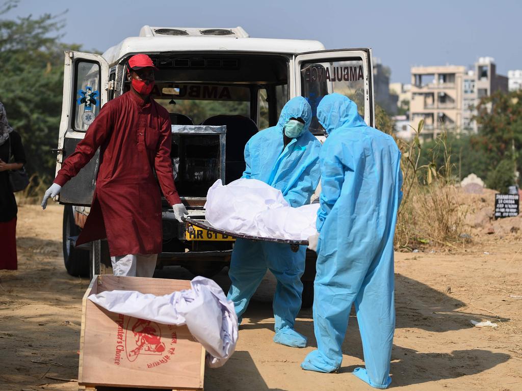 Health workers wearing personal protective equipment suits prepare to place the body of a coronavirus victim in a coffin at a graveyard in New Delhi. Picture: AFP