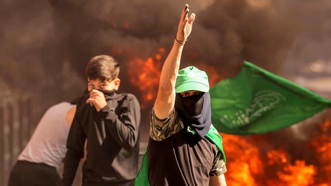 A masked Palestinian protester gestures while walking near flaming tires during clashes with Israeli forces following a rally in solidarity with Gaza by supporters of the Fatah and Hamas movements, in the city of Hebron in the occupied West Bank on October 13, 2023. AFP correspondents and a security official reported clashes after rallies in solidarity with war-battered Gaza in Ramallah, Nablus, Tulkarm, Hebron and other cities and towns, with the Palestinian Red Crescent reporting dozens wounded across the West Bank, some critically. (Photo by HAZEM BADER / AFP)