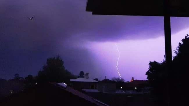 A plane flies over amid a lightning storm, as seen from North Adelaide. Picture: Kate Jarmyn