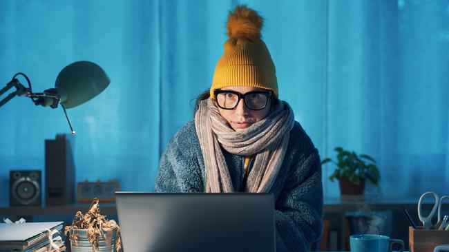 Woman sitting at desk and feeling cold, she is wearing warm clothes and saving money on her utility bills, electricity generic winter