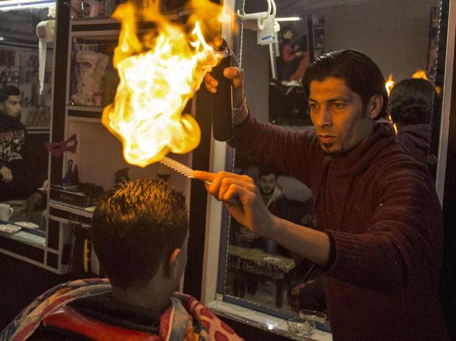 Ramadan Edwan, a Palestinian barber, uses fire in a hair-straightening technique with a client at his salon in the Rafah refugee camp, in the southern Gaza Strip on February 1, 2017. / AFP PHOTO / MAHMUD HAMS