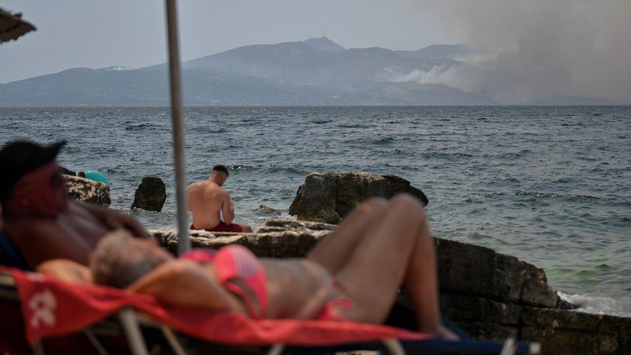 People sunbath near the coastal town of Saranda on the Albanian Riviera as smoke billows from the Greek Island of Corfu on July 25, where authorities evacuated nearly 2500 people the day before. Picture: Armend Nimani / AFP