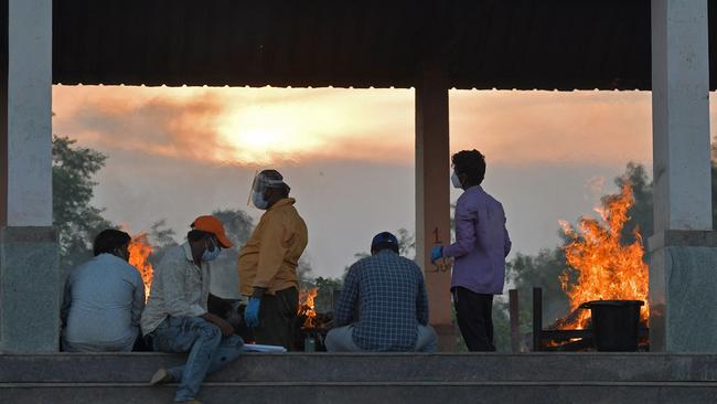 People are seen next to burning pyres of victims who lost their lives due to the coronavirus at an open crematorium in Bangalore, India. Picture: Manjunath Kiran / AFP