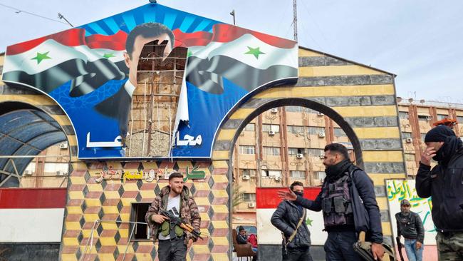 Anti-government fighters stand in front of a defaced portrait of Syrian President Assad, as they patrol a street in the Syrian southern city of Daraa on December 7, 2024. Picture: AFP