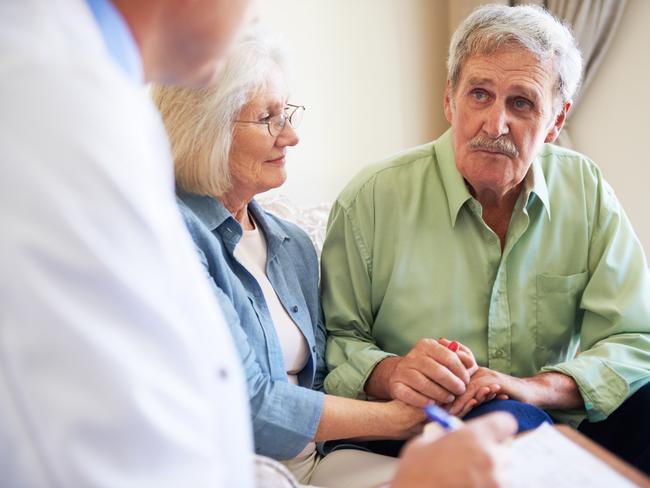 A senior man holding his wife's hand and listening to his doctor