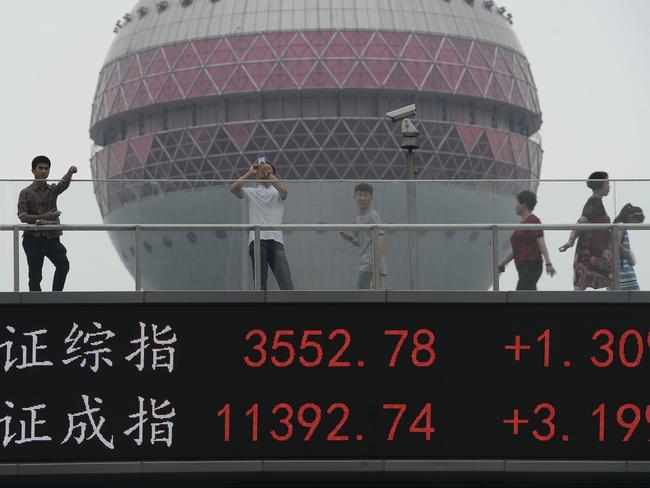 People walk on a footbridge with an electronic stock ticker.