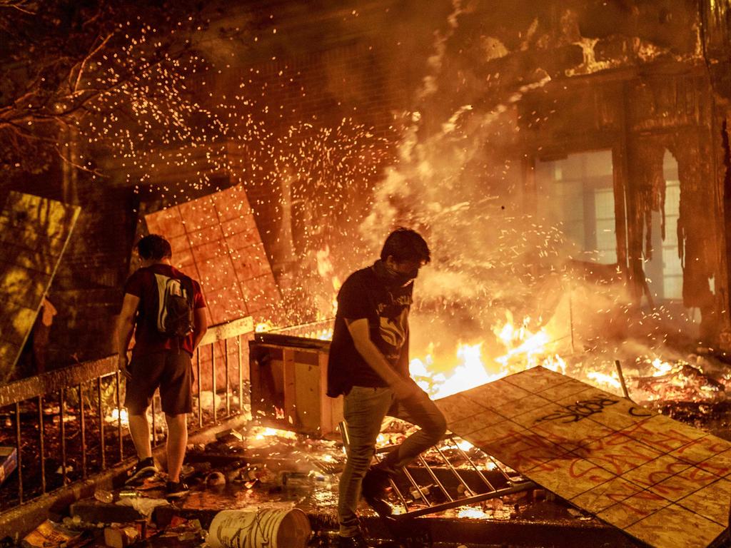 Protesters walk past burning debris outside the Third Police Precinct in Minneapolis that was set on fire by protesters. Picture: Kerem Yucel / AFP.