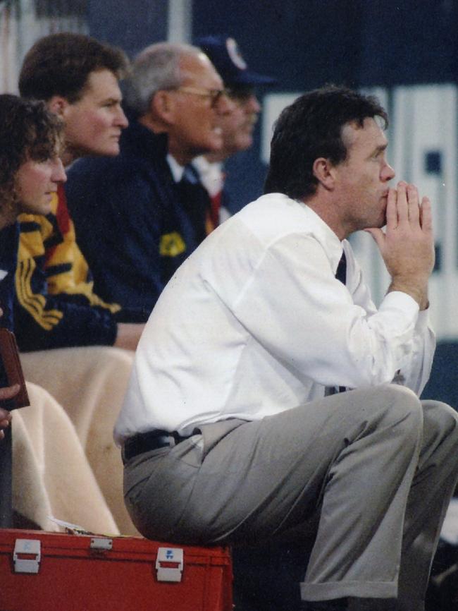 Crows coach Robert Shaw sitting on the edge of box in front of bench in 1995.