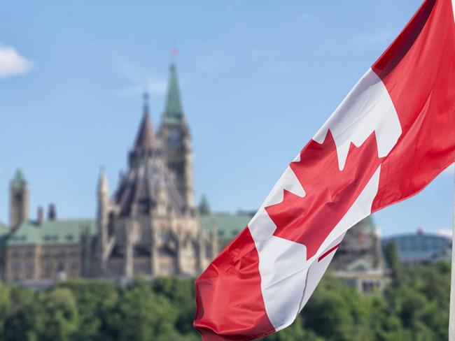 Canadian flag waving with Parliament Buildings hill and Library in the background. Picture: iStock.