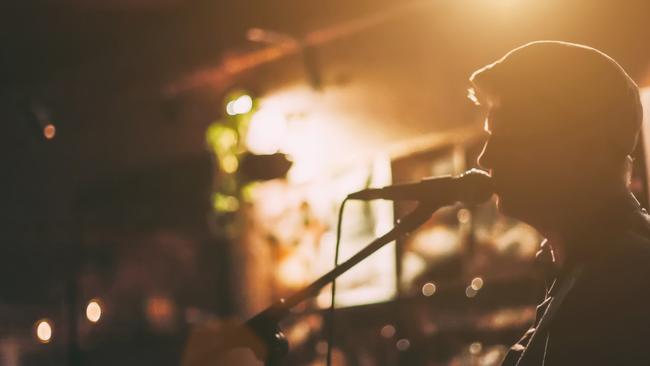 A male singer on a stage performing with guitar at a bar generic, music, microphone, shadow. Picture: iStock