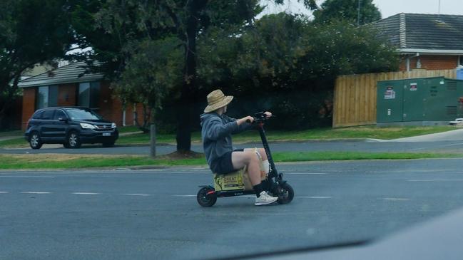 An e-scooter rider using a slab of beer as a seat zooms across the Surf Coast Highway at Torquay.