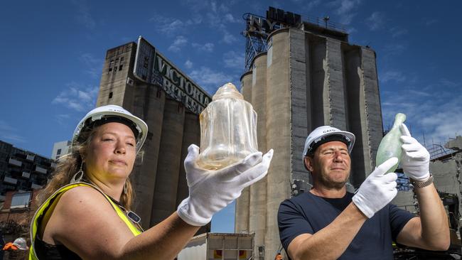 Archaeologist Liz Hawksley and Caydon boss Joe Russo hold up a glass decanter and torpedo bottle uncovered at the site. Picture: Jake Nowakowski.