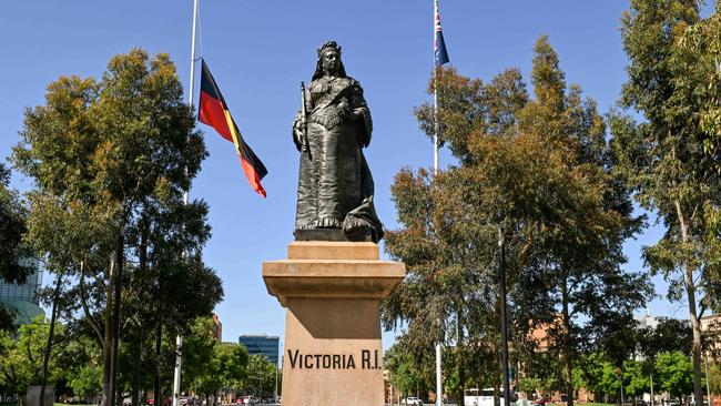 ADELAIDE, AUSTRALIA - NewsWire Photos October 18, 2023: A statue of Queen Victoria in front of the Aboriginal flag at half mast and the Australian flag at full staff in Victoria Square. The Adelaide city council has decided to fly the Aboriginal flag at half-mast on the Town Hall and in Victoria Square after SaturdayÃs referendum defeat. Picture: NCA NewsWire / Brenton Edwards