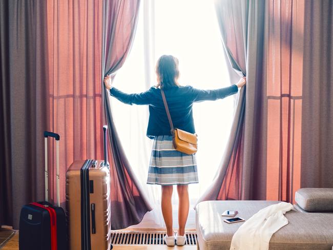 ESCAPE: Rear view of tourist in the hotel room pulling the curtains to see the view. Picture: Istock