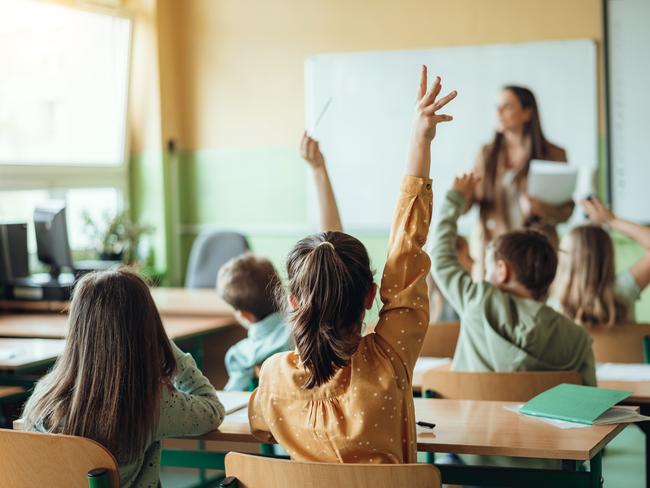 Students raising hands while teacher asking them questions in classroom
