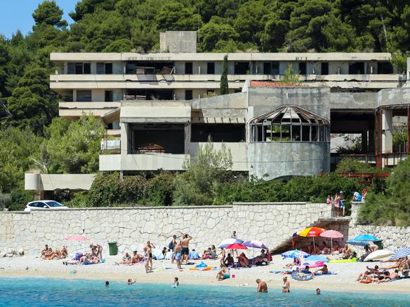 Kupari, Croatia - July 18, 2017 : People swimming and sunbathing on a sea beach next to an old building of hotel Gorcina in Kupari, Croatia.