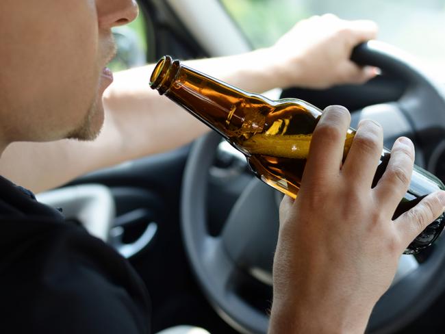 The concept of alcohol driving crime - closeup of young male driver hands with steering wheel and bottle of beer. Drink driving generic. Picture: iSTOCK