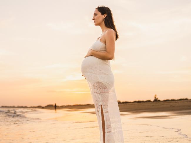 beautiful pregnant woman dressed in white standing on the shore of the beach looking at the sea