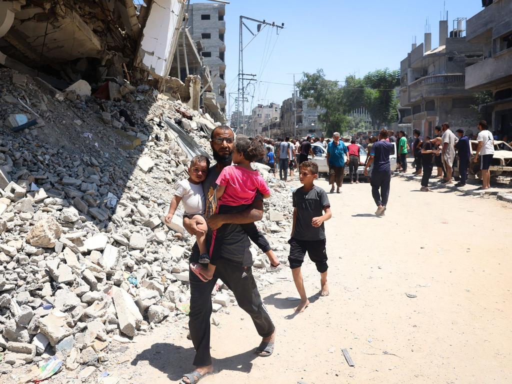 A man carries children as people past damage following Israeli bombardment at al-Bureij refugee camp in the central Gaza Strip on July 23. Picture: AFP