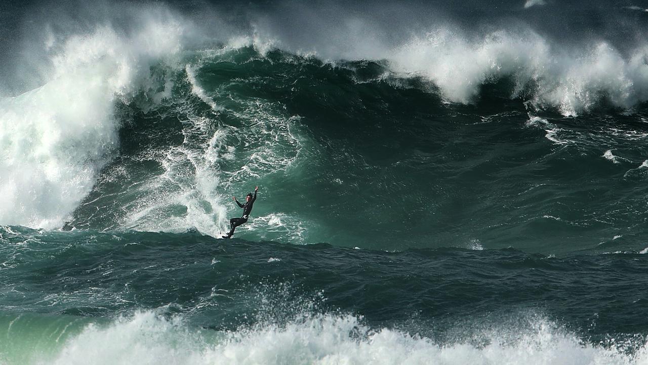 A couple of guys take turns riding a jet ski while the other surfs the huge swell. Picture: John Grainger