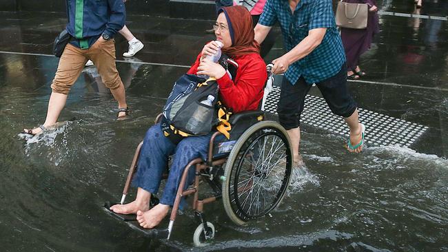 A man pushes a lady in her wheelchair across Flinders Street. Picture: Ian Currie